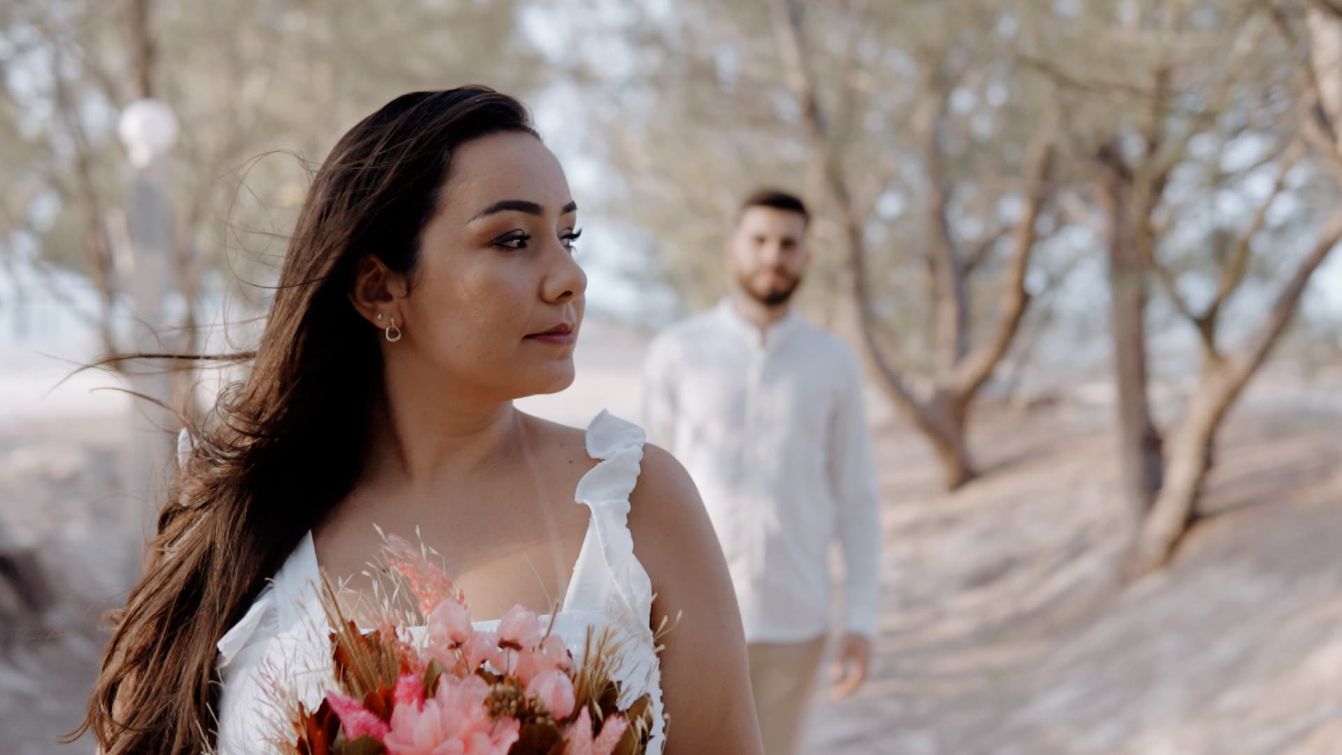 Noiva com buquê e noivo de fundo